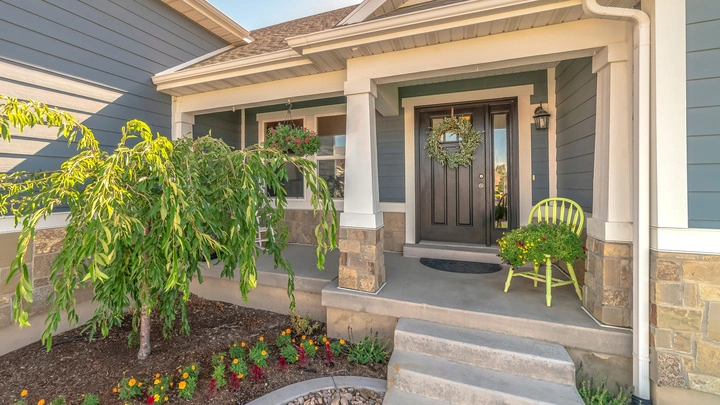 Landscape design for front yard featuring a small tree, colorful flower bed, and a welcoming stone-accented porch with a decorative chair by Hawkins Landscaping.