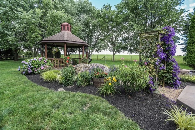 Landscaping with a gazebo, vibrant flowers, and lush greenery in a beautifully designed backyard by Hawkins Landscaping.
