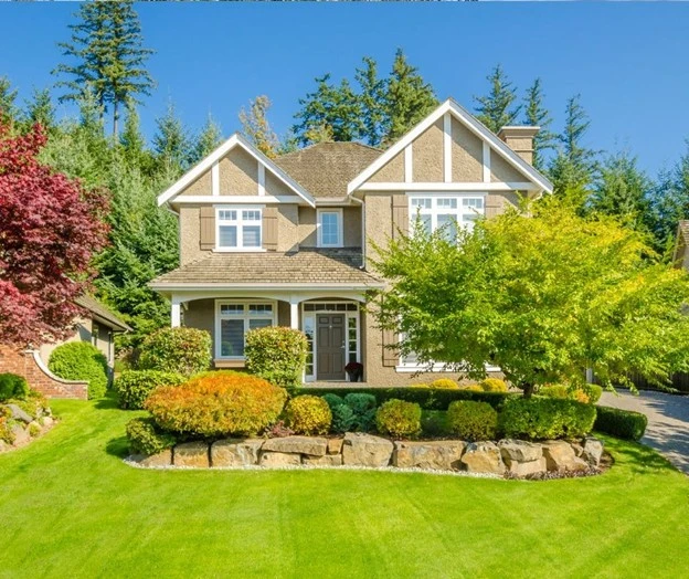 Beautiful front yard featuring landscaping with rocks, green lawn, and colorful fall shrubs in front of a modern suburban home.