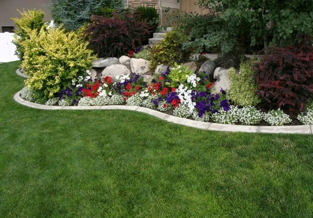 Colorful flower bed with curved rock border and lush green lawn, showcasing expert landscaping with rocks by Hawkins Landscaping.