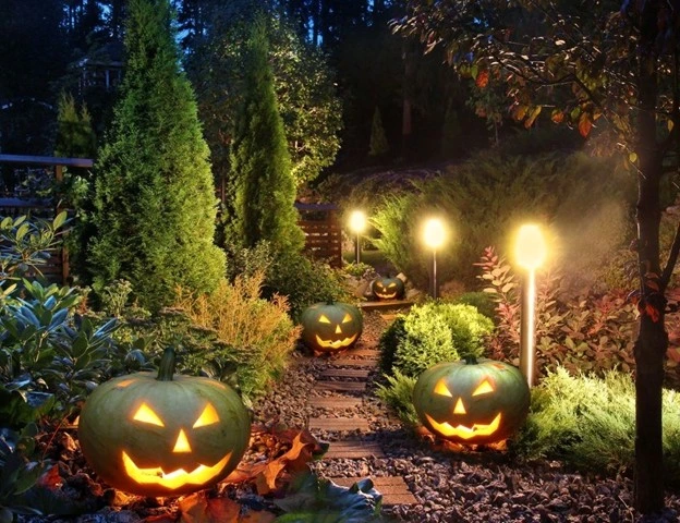 Glowing jack-o’-lanterns line a stone garden path surrounded by lush greenery and landscape lighting, showcasing creative landscaping ideas for front yard Halloween décor by Hawkins Landscaping.