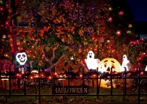 A festive yard decorated with Halloween-themed landscaping lights by Hawkins Landscaping, featuring glowing pumpkins, ghosts, and a skeleton surrounded by colorful string lights and trees.