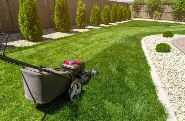 A lawn mower cutting thick green grass in a well-kept backyard, showcasing the clean, professional results of a lawn care specialist by Hawkins Landscaping.