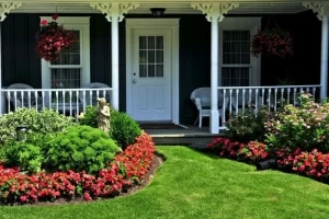 Charming garden with lush green lawn, colorful flower beds, statues, hanging plants, and a white archway, showcasing landscaping ideas for front yard by Hawkins Landscaping.