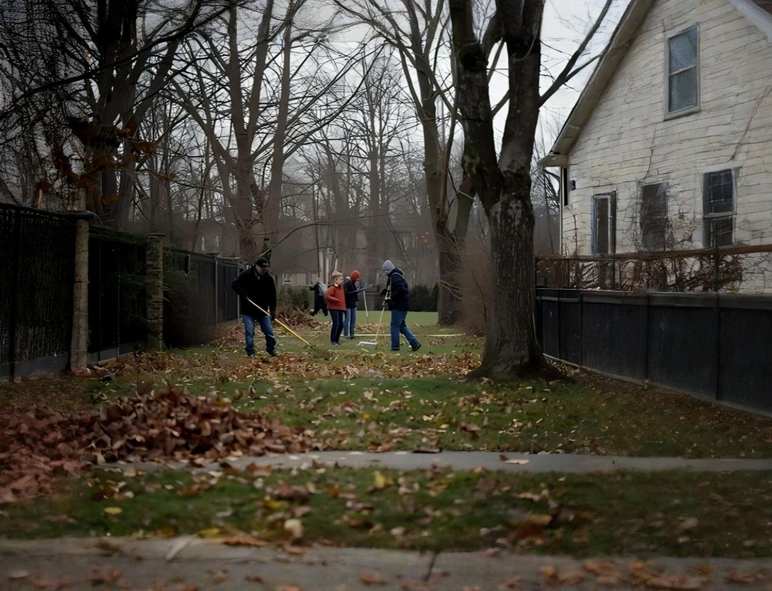 People performing Fall Cleanup by raking leaves in a backyard, showing seasonal yard maintenance services similar to what Hawkins Landscaping Inc provides.