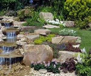 Tiered stone waterfall and garden bed showcasing expert landscaping design with natural boulders and colorful plantings by Hawkins Landscaping.