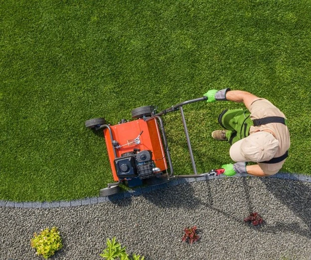 Landscape maintenance in progress with a professional mowing a neatly edged lawn using commercial equipment by Hawkins Landscaping.