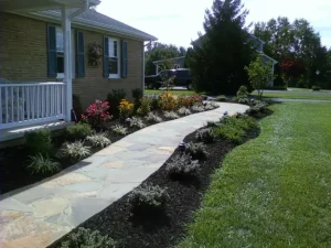 Landscaping ideas featuring a curved stone walkway, colorful flower beds, and neatly mulched garden borders enhancing a front yard by Hawkins Landscaping.
