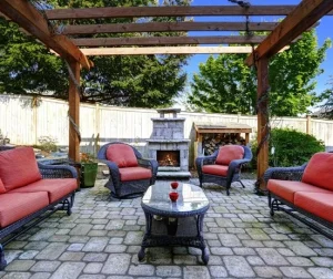 Patio with pavers by Hawkins Landscaping featuring a cozy outdoor seating area under a wooden pergola with a fireplace and stone paver surface.