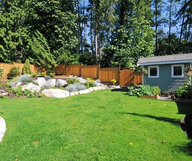 Lawn maintenance services by Hawkins Landscaping featuring a large, healthy green lawn with neatly maintained landscaping, decorative boulders, shrubs, and trees that enhance curb appeal and outdoor beauty.