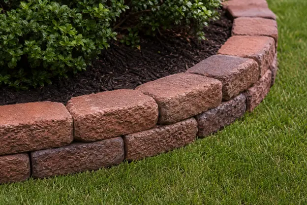 Landscaping bricks by Hawkins Landscaping forming a curved garden border that neatly separates a mulched planting bed with shrubs from a healthy green lawn for a clean, finished landscape design.